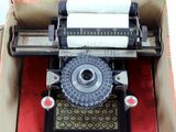 une vieille machine à écrire dans une boîte, sur laquelle est posé un rouleau de papier