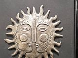 a picture of a metal sun face in a black frame