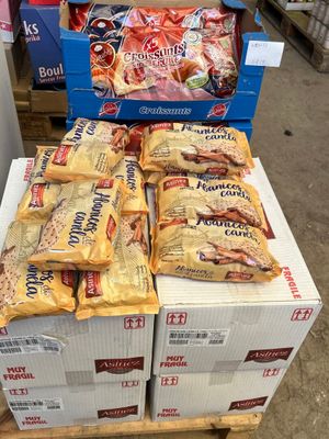 Plusieurs cartons de snacks sont empilés sur une palette dans un magasin.