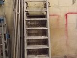 une échelle appuyée contre un mur, à côté d'un tas de tuyaux métalliques