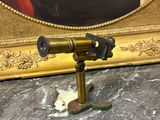 un télescope ancien en laiton posé sur une table en marbre, avec un tableau en arrière-plan