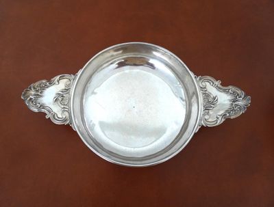 an antique silver plate with a handle on a brown table