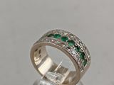 a close up of a diamond and emerald ring on a clear surface