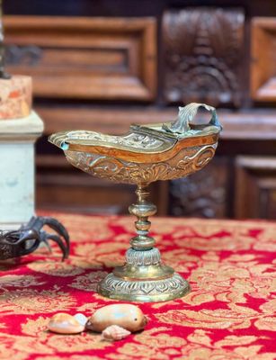 un bol en or posé sur une nappe rouge, à côté de quelques coquillages