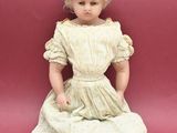 doll sitting on the floor in a white dress on a pink background