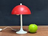a red table lamp next to an apple on a wooden table