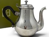 the teapot is silver with a black handle and a green box