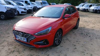 La voiture rouge est garée sur un parking, avec d'autres voitures en arrière-plan.