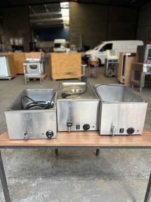 trois casseroles en acier inoxydable posées sur une table dans un entrepôt