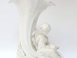 un vase blanc posé sur une table, sur laquelle est assise une femme