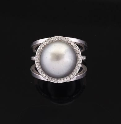 a white pearl and diamond ring on a black surface