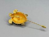 broche dorée surmontée d'une tortue, posée sur un fond gris