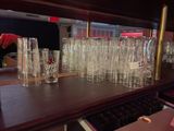 a lot of glasses on the bar with a man in the background