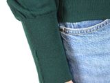 a woman in a green sweater and jeans holding a cell phone