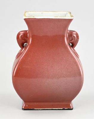 un vase rouge à deux anses posé sur une surface blanche