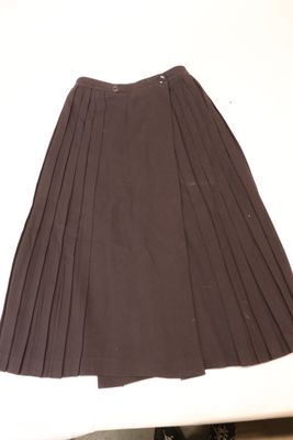 une jupe plissée marron posée sur une table, à côté d'une paire de chaussures noires