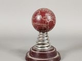 une boule de marbre rouge posée sur un socle en métal