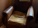 un fauteuil en cuir marron, avec un coussin posé dessus, devant une fenêtre