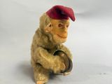 un petit singe en peluche coiffé d'un bonnet rouge, assis sur un tonneau