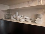 many white dishes and cups on a shelf in the kitchen