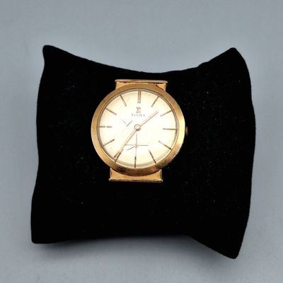 une montre en or posée sur un coussin noir, sur une table