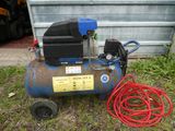 a blue compressor sitting on the grass next to a red hose