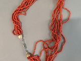 an orange beaded necklace with a gold clasp on a gray surface