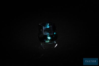 un gros plan d'une bague dans l'obscurité, ornée d'une pierre verte qui brille