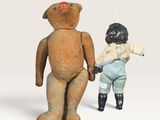 un petit ours en peluche et une petite poupée, debout l'un à côté de l'autre
