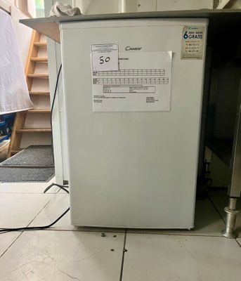 un réfrigérateur blanc dans une pièce, avec un escalier en arrière-plan