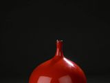 un vase rouge posé sur une table près d'un mur noir