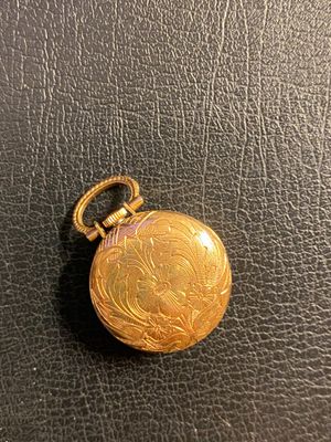 une image représentant une montre de poche en or posée sur une surface en cuir noir
