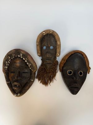 trois masques africains accrochés à un mur, devant lesquels se tient une personne
