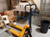 many boxes on the floor of a warehouse with a hand truck