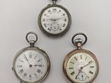 trois types différents de montres de poche posées sur une surface blanche