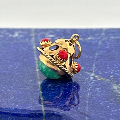 a gold ring with a green and red bead on a blue surface