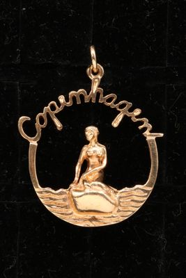 a close up of a gold pendant with a woman on a surfboard