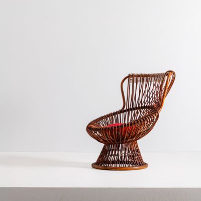 Une vieille chaise en osier, avec un coussin rouge, est posée sur une surface blanche.