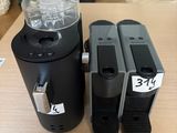 two black coffee machines sitting on top of a table next to a plant