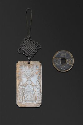 deux pendentifs chinois en argent et une pièce de monnaie sur un fond noir