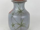 a blue vase with green leaves on it on a white surface
