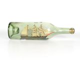 une bouteille en verre contenant un bateau, posée sur une surface blanche