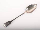 une cuillère en argent à long manche posée sur une surface blanche