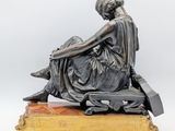an antique bronze statue of a woman sitting on a bench