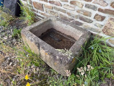 un abreuvoir en pierre posé dans l'herbe, près d'un mur de briques