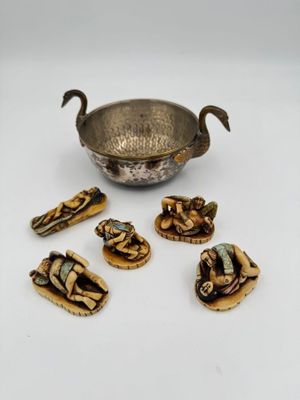 une image représentant un bol en argent et six petites figurines posées sur une surface blanche