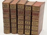 five old books are lined up in a row on a white surface