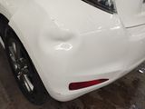 the rear end of a white car in a garage with other cars in the background