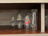 bottles and glasses are lined up on a shelf in a kitchen