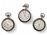 three antique pocket watches are displayed on a white surface